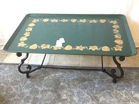 Full view of coffee table with green tray top and wrought iron base on floral carpet.