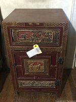 Front view of the small red lacquer cabinet showing carved detailed drawer and cabinet door with metal hinges.