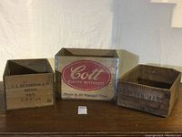 Three vintage wooden crates positioned side by side showing different sizes and branding (Cott, Gloag's Perth Whisky, C.L. Richardson & Co).