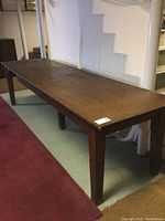 Photo showing entire length of the vintage wood workbench against a wall, highlighting the solid wood top and legs with visible wear and patina.