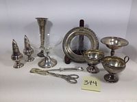 Overview of ten sterling silver and glass tableware items including compotes, vase, creamer set, salt and pepper shakers, tongs, cheese cutter