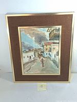 Framed watercolor painting showing a street scene with a solitary figure and buildings. The frame is metallic with a brown textured mat.