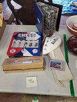 Overview of lot including chess set tin, deflated Patriots football, cardboard box for baseball puzzle, and binder with sports cards.