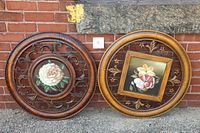 Both round floral metal wall hangings leaning against brick wall showing overall size and design difference