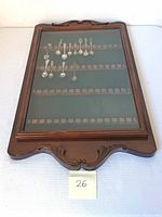 Full view of wooden display case with glass front showing 14 souvenir spoons mounted inside with green felt backing.