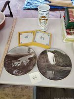 Two Royal Doulton scenic photo collector's plates, two vintage Dutch ceramic tiles mounted on wood, and one Italian Cicer Nig decorated vase displayed on a table