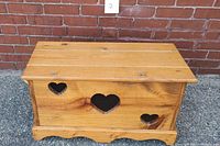 Front of vintage pine chest showing heart-shaped cutouts with black mesh and scalloped base trim.