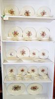 Shelves displaying Wedgwood china dinner plates, cake plates, teacups, bouillon cups with saucers, and serving platters, all with floral decoration.