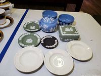 Photo showing collection of blue, green, and black Wedgwood jasperware and cream Edme pattern ashtrays arranged on table.