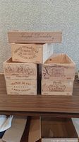 Photo showing six wooden wine crates stacked, each with vintage wine branding including Joseph Drouhin, Château Margaux and others.