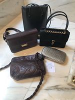 Five assorted handbags and clutches placed on a marble surface: two black handbags, two brown purses, and one silver clutch.