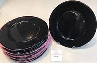 Stack of black plates with one plate displayed on stand and lot card