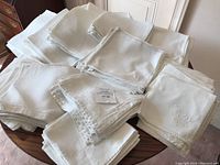 Photo showing multiple stacks of folded white linen napkins of different styles and sizes including embroidered, damask, and hemstitched.