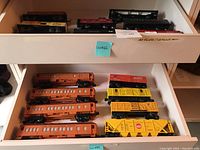 Wide angled photo showing 16 model train cars arranged in drawers with visible orange passenger cars and yellow freight cars.