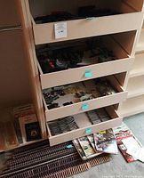 Multiple trays on shelving containing assorted Lionel train tracks, switches, parts, and accessories. Curved and straight track sections are visible along with instruction manuals and packaging.