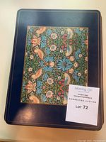 Single placemat with dark blue border and central floral and bird pattern, held flat on table.