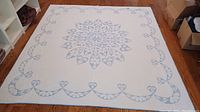 Full view of the white queen sized quilt with blue floral applique pattern laid out on floor.
