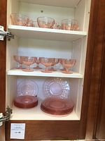Glassware set displayed in shelving, showing teacups on top shelf, ice cream coupe glasses on middle shelf, dessert plates and saucers on bottom shelves.