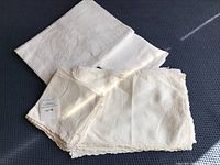 Photo showing folded white hand-embroidered linens including napkins and part of the tablecloth with floral embroidery and lace edges
