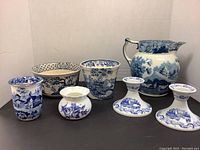 Full lot front view showing two candlesticks, two small vases, two bowls, and pitcher with blue and white designs on black surface