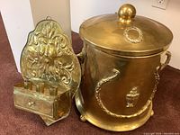 Photo showing both the large brass pail with lid and the lion head wall hanging candle holder together for scale and detail.