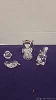 Four clear crystal animal figurines on dark blue surface including an angel with gold halo, squirrel with broken foot, and two birds, one with detached piece.