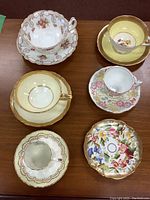 Top view of five cups with matching saucers and one extra saucer, showing floral and gold designs on porcelain.