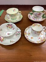 All four sets of floral cups and saucers arranged on a wood surface showing designs and shapes.