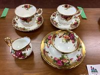 Front view of the set showing 2 Royal Albert cups and saucers, 2 side plates and 1 creamer with floral and gold detailing