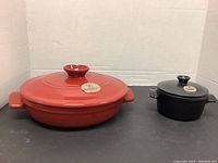 Two Emile Henry lidded casserole dishes, one red and larger, one black and smaller