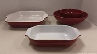 Two rectangular Emile Henry casserole dishes in red exterior and white interior together with two red circular bowls, one nested inside the other, showing the assortment in the lot.