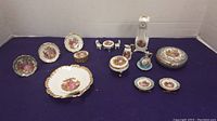 Full assortment of miniature Limoges porcelain dishes and decorative items displayed on purple cloth background.
