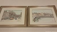 Two framed pen and ink drawings with light color washes side by side on wall