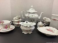 Complete tea set including teapot, six small bowls, cup with saucer, sugar bowl with lid, cream pitcher and serving plate. Floral rose design with gold accents.