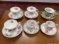 Overview of all 6 Royal Albert cups and saucers showing different floral patterns and gold trim on a wooden table.