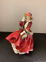 Front view of the Royal Doulton figurine showing the woman in red dress with hat lifting it slightly.