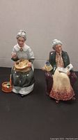 Two Royal Doulton figurines displayed side by side, 'Prized Possessions' and 'Embroidering'