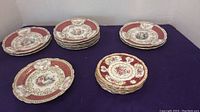 Multiple stacks of the red and gold small plates with Lady Hamilton classical figures in the center, seen from above