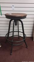 Front view of the industrial style stool showing the round wooden seat and metal legs with footrest rings.