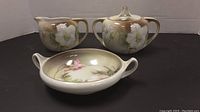 Photo showing the sugar bowl with lid, creamer, and small two-handled serving bowl from the front angle, displaying floral patterns.