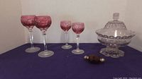 4 red cut glass wine glasses, 2 sizes, arranged on table with purple lidded candy dish and red salt and pepper shaker pair.