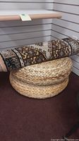 Two round woven wicker decor pieces stacked with a rolled patterned rug on top.
