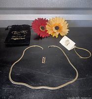Complete jewelry set with pendant, chain, bracelet, and packing bag on black surface, flowers in background