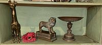 Shelf display of the brass giraffe, brass lion on a base, and bronze tazza pedestal showing relative sizes and arrangement.