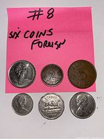 Front view of all six foreign coins arranged on pink paper with '#8 six coins foreign' written.