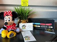 Photo showing the Minnie Mouse plush with a red polka dot dress and bow, yellow shoes, two commemorative Disney pins in packaging, and four Invicta Disney polka dot watchbands in leather displayed in a case.
