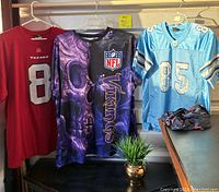 Three hanging NFL football jerseys including Texans, Vikings, and Lions.