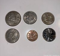Top side view of six foreign coins on white background, showing coat of arms, animal figures, and inscriptions