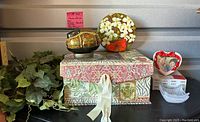 Wide view of all items including lacquer box, floral round lid, heart photo frame, glass candle holder, faux greenery, and decorative card.