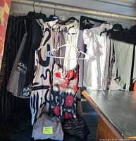Photo of various ladies' garments hanging on a rack including black and white patterned dresses, black jacket with patterned cuff, white blouse, and black and white pants.